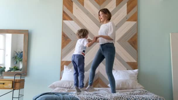 Des enfants excités sautent sur le lit. Jeune maman active sautant avec son fils Le matin . — Video