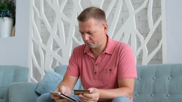 Junger Kaukasier nutzt Smartphone für Online-Einkäufe mit Kreditkarte im Wohnzimmer. . — Stockvideo