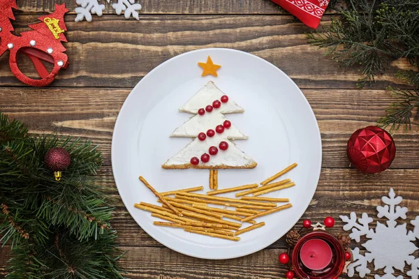 Kreatywne jadalne choinki, sztuka jedzenia. Jedzenie dla dzieci i świąteczny stół. Drzewo z chleba z serem śmietankowym ozdobione jagodami na białym talerzu na drewnianym tle. — Zdjęcie stockowe