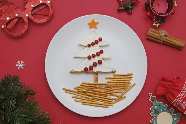 Kreatywne jadalne choinki, sztuka jedzenia. Jedzenie dla dzieci i świąteczny stół. Drzewo z chleba z serem śmietankowym ozdobione jagodami na białym talerzu na czerwonym tle. — Zdjęcie stockowe