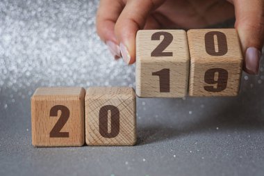 Yeni yıl 2019 'dan 2020' ye geçiş. Gümüş arkaplandaki tahta bloğu elle çevir