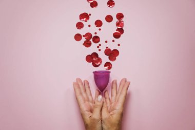 Kırmızı parçacıklı regl kupası ve pembe arka planda kadın eli, gezegenin kadın sağlığı ve ekolojisi kavramı.