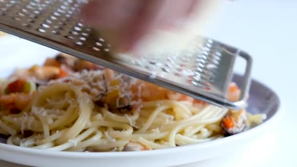 Готовить макароны с морепродуктами. Сыр на терке, типичный итальянский сыр, макароны на тарелке только что приготовленные — стоковое видео