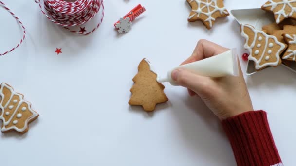 Hacer galletas de jengibre para Navidad. Pintura a mano para mujer con esmalte blanco en galletas. Vista superior — Vídeo de stock