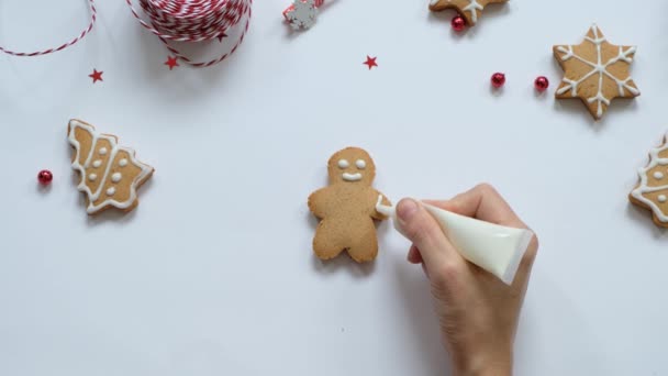 Lebkuchen backen zu Weihnachten. Frauenhandbemalung mit weißer Glasur auf Plätzchen. Ansicht von oben — Stockvideo