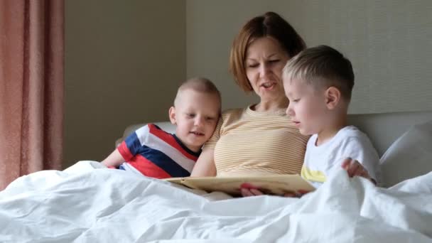 Madre leyendo un libro a sus hijos niños pequeños en la cama, cuidando a un niño — Vídeos de Stock