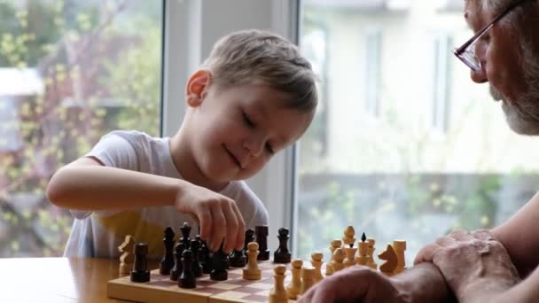 Niño pequeño jugar ajedrez con su abuelo, hombre positivo senior — Vídeos de Stock
