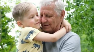 Küçük çocuk büyükbabasına sarılıyor ve onunla konuşuyor. Yetişkin bir adam, dışarıda parkta oturuyor.