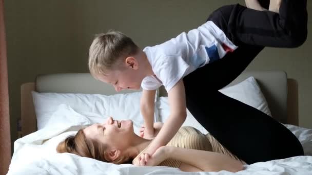 Lycklig mor har kul med sin son pojke på en säng, spelar flygande plan — Stockvideo