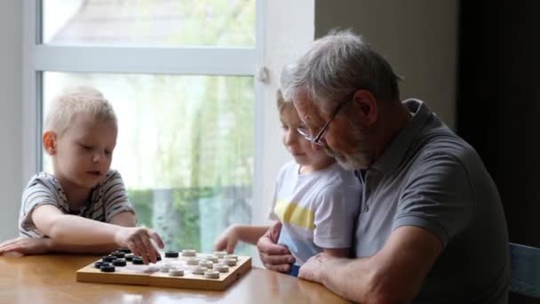 Anak-anak kecil bermain catur dengan kakek di rumah, pria senior yang positif — Stok Video