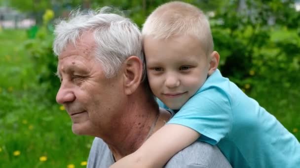 Küçük çocuk büyükbabasına sarılıyor, olgun bir adam, dışarıda parkta oturuyor. — Stok video