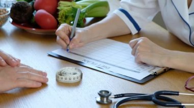 Doktor beslenme uzmanı hastaya danışmanlık yapıyor ve diyet beslenme planı yazıyor.