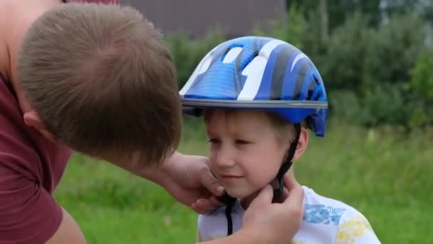 Vader zet veiligheidshelm op z 'n zoons hoofd... en leert de gelukkige jongen fietsen. — Stockvideo