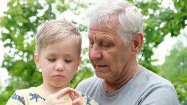 Küçük çocuk büyükbabasına sarılıyor ve onunla konuşuyor. Yetişkin bir adam, dışarıda parkta oturuyor.