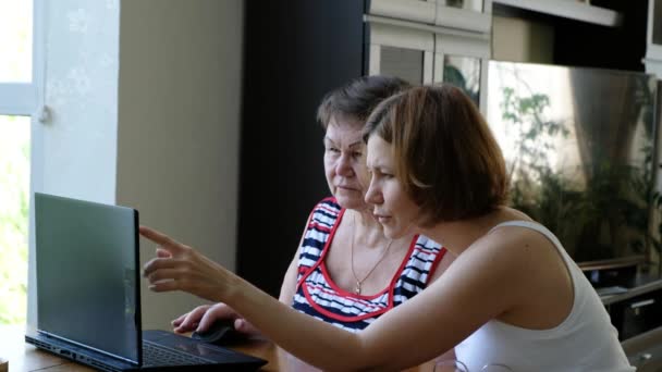 Dorosła córka pomaga starszej kobiecie, jej matce, przy pomocy laptopa — Wideo stockowe