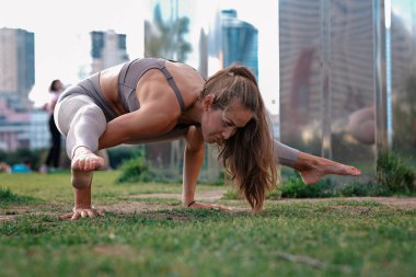 Arka planda şehirle yoga egzersizleri yapan genç bir kadın. Güzel Asana ellerinde