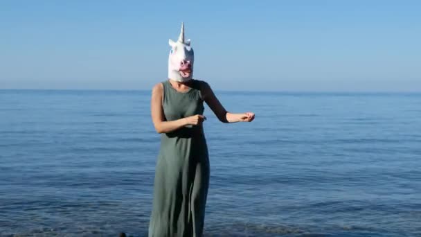 Mulher com unicórnio cabeça máscara dançando junto ao mar, estranho engraçado estranho vídeo. — Vídeo de Stock