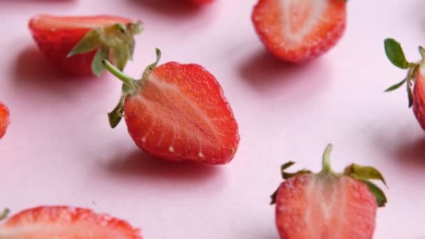 핑크 빛 회전 배경에 즙이 많은 딸기 반쪽이 위에서 바라본 모습 — 비디오