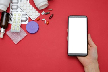 İnternette eczane ve eczane kavramı. Kırmızı arka planda ilaç ve akıllı telefon var.