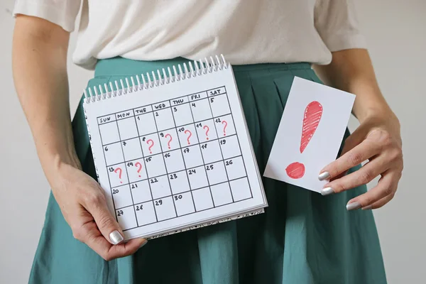 Takvimde işaretli bir boşluk ve ünlem işareti olan bir kadın. İstenmeyen hamilelik ve adette gecikme.