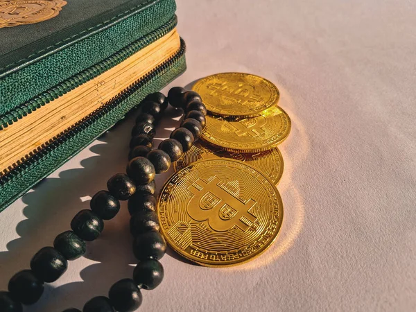 Yeşil bir cüzdanın yanına yerleştirilmiş üç altın Bitcoin para ve beyaz arka planda siyah tespih (tasbih).
