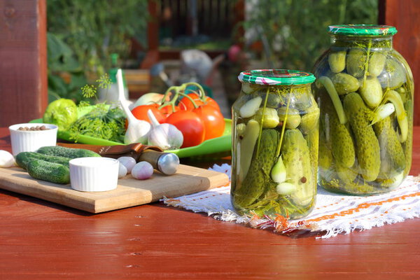 Canning cucumbers with spices in glass jars on a wooden table in front of the greenhouse.