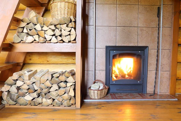 Wood stove and firewood in rural wooden house. Part of  the room interior in a rural house with a stack of firewood and  a stove with burning wood.