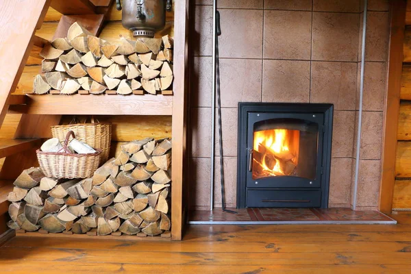 Wood stove and firewood in rural wooden house. Part of  the room interior in a rural house with a stack of firewood and  a stove with burning wood.