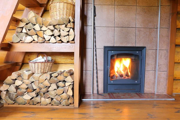 Wood stove and firewood in rural wooden house. Part of  the room interior in a rural house with a stack of firewood and  a stove with burning wood.