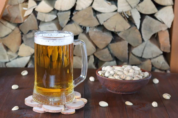 Mug of light beer on the table against the background of firewood.