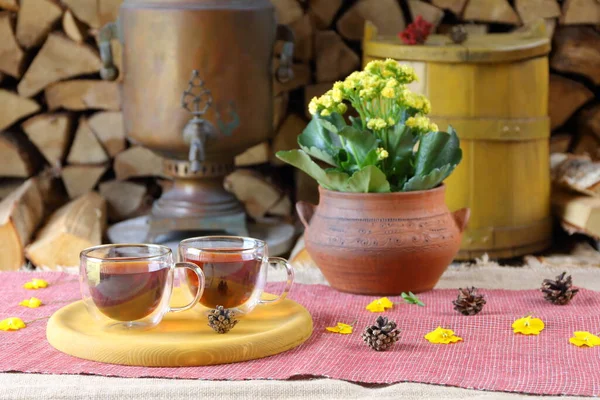 サモバー 黄色の浴槽と薪のスタックの背景に紅茶のカップルガラスマグカップ — ストック写真