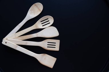 Siyah arka planda kaşık ve spatulalar da dahil olmak üzere bambu mutfak aletleri koleksiyonu. Doğal çevre dostu ahşap aletler yemek pişirmek, yemek servisi yapmak ve sürdürülebilir bir yaşam tarzını desteklemek için.