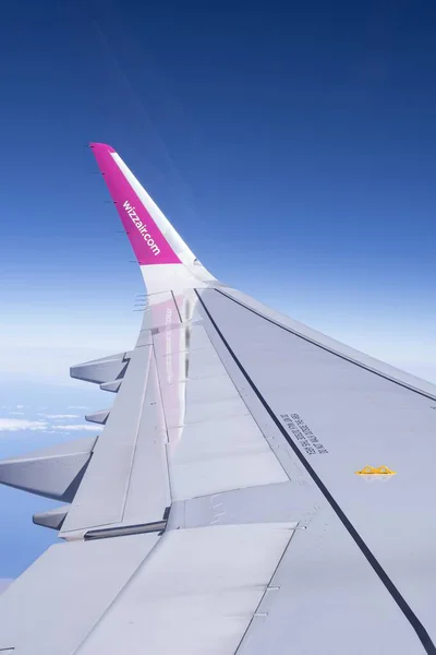 Okyanus ve bulutların üzerinde kanat kanadı olan uçak kanadı yakın görüntüsü. Yolcu penceresi perspektifi mavi gökyüzü altında kıyı şeridi üzerinde uçuşu gösteriyor.