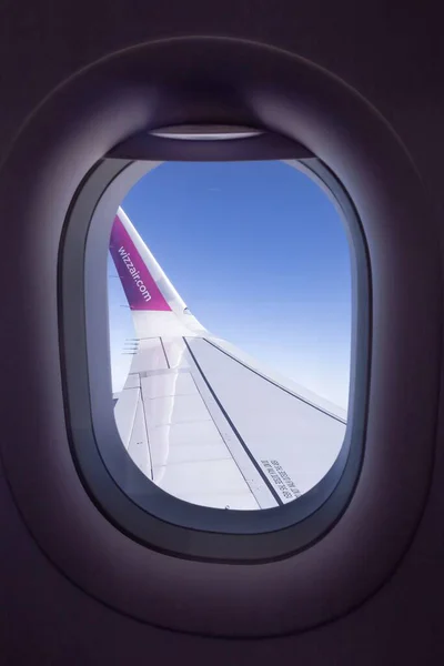 Okyanus ve bulutların üzerinde kanat kanadı olan uçak kanadı yakın görüntüsü. Yolcu penceresi perspektifi mavi gökyüzü altında kıyı şeridi üzerinde uçuşu gösteriyor.