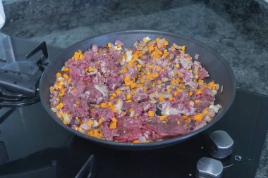 Kızartma tavasında çiğ et ve sebze. Taze doğranmış soğan ve et parçaları pişirilmeye hazır havuçla birlikte siyah bir mutfak sobasına konuldu. Sağlıklı ev yapımı gıda geçmişi.