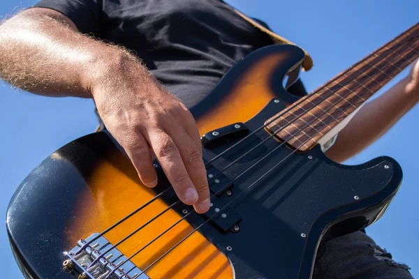 Man play electric bass guitar against blue sky