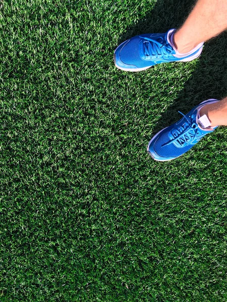 Stadyumun kırmızı koşu bandında mavi spor ayakkabılı bir adam koşuyor.