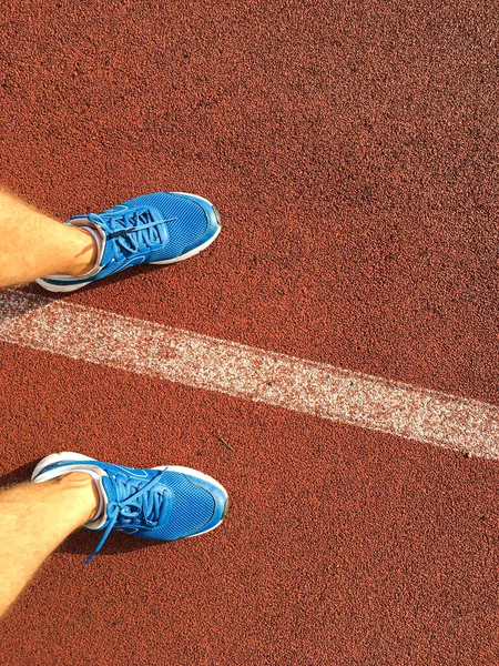 Stadyumun kırmızı koşu bandında mavi spor ayakkabılı bir adam koşuyor.