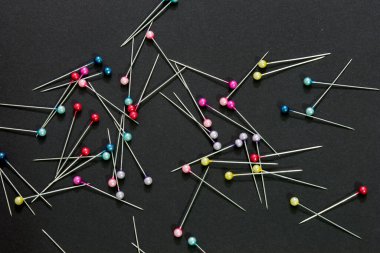 Bu siyah arkaplana yerleştirilmiş renkli dikiş iğnelerinin fotoğrafı.