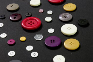 Bu siyah arkaplandaki renkli dikiş düğmelerinin fotoğrafı.