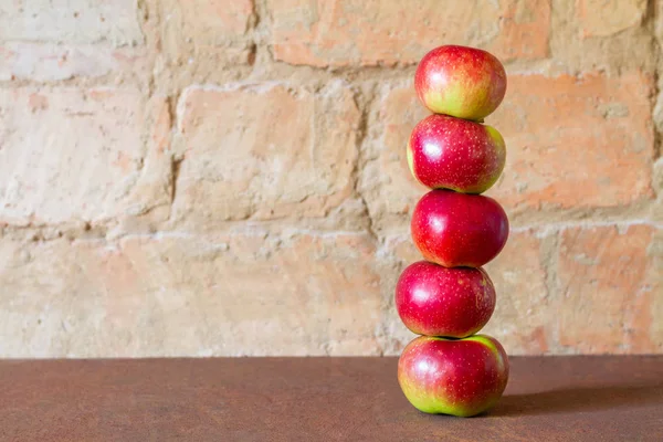 Tower of five fresh red apples on the brick wall background. Closeup, selective focus