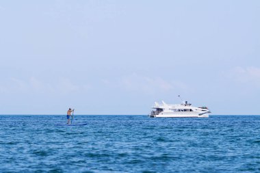 Bir adam denize binerken ayağa kalkamaz. SUP, ayağa kalk. Denizde beyaz bir zevk teknesi.