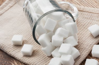 Cam bir fincanda ve bej havlunun üzerinde beyaz şeker küpleri. Yakın çekim, seçici odaklanma