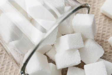 Cam bir fincanda ve bej havlunun üzerinde beyaz şeker küpleri. Yakın çekim, seçici odaklanma