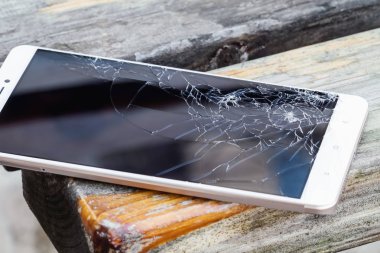 Ekranı kırık akıllı telefon ahşap bankta yatıyor. Seçici odak