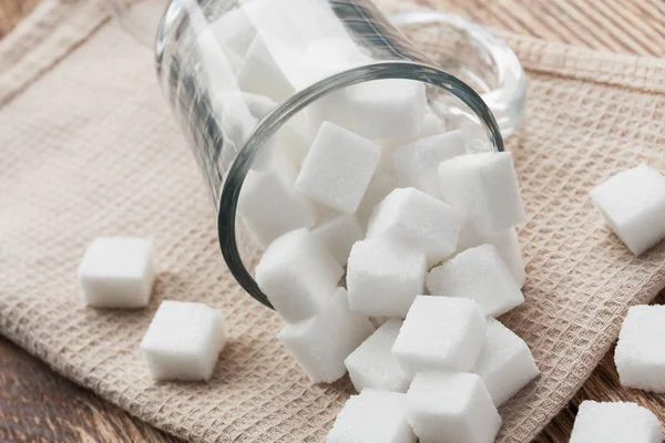 Cam bir fincanda ve bej havlunun üzerinde beyaz şeker küpleri. Yakın çekim, seçici odaklanma