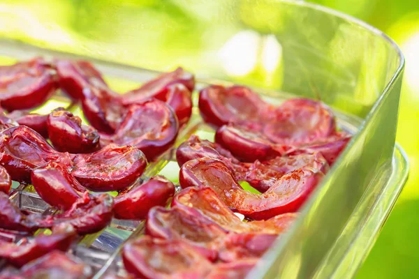 Çiçek arkaplanındaki kurutucuda kiraz var. Susuz bırakma tepsisinde kiraz yarıları. Yakın çekim, seçici odaklanma