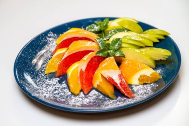 Mavi bir tabakta dilimlenmiş portakal, greyfurt, elma ve nane yaprağı.