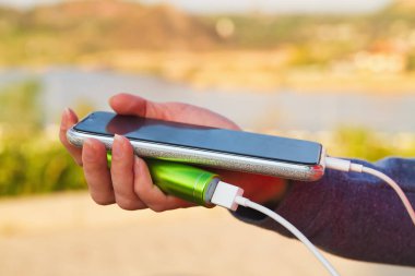 Bir kız dış güç bankasından şarj olurken açık havada akıllı telefon kullanıyor.