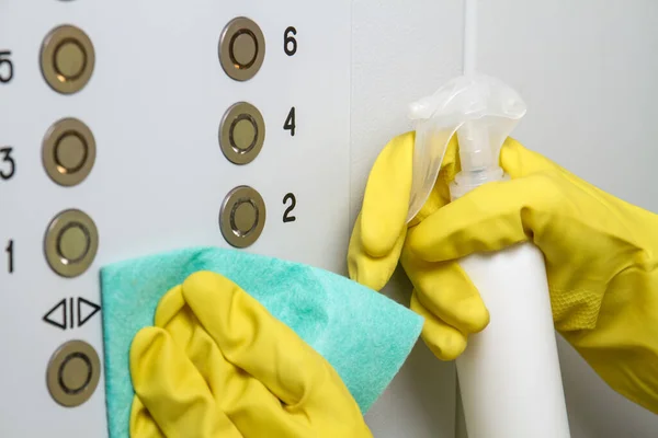 Paçavra ve spreyli eldiven giyen eller asansör düğmelerini temizliyor. Dezenfeksiyon kavramı.